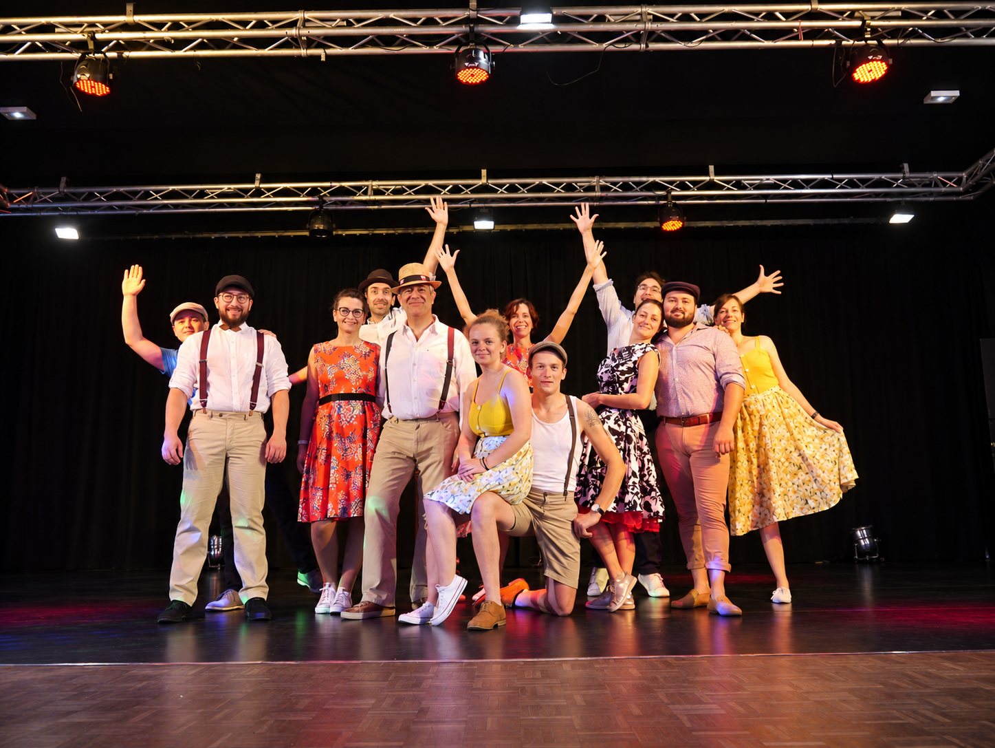 Un groupe de danseurs en tenues rétro pose, bras levés, sur la scène du gala.